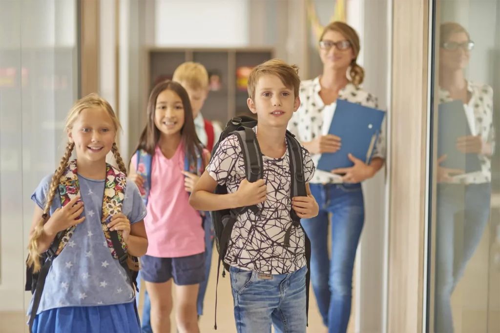 Children with backpacks walking with an adult in a school hallway